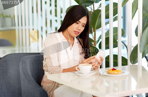 Image of asian woman with smartphone and earphones at cafe