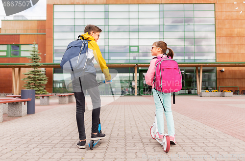 Image of school children with backpacks riding scooters