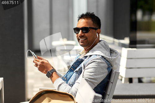 Image of man with earphones and smartphone on city street