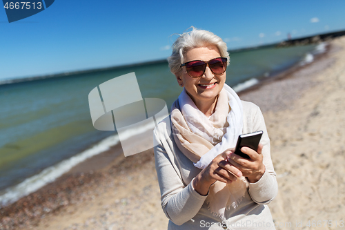 Image of senior woman using smartphone on beach