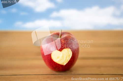 Image of red apple with carved heart shape on wooden table