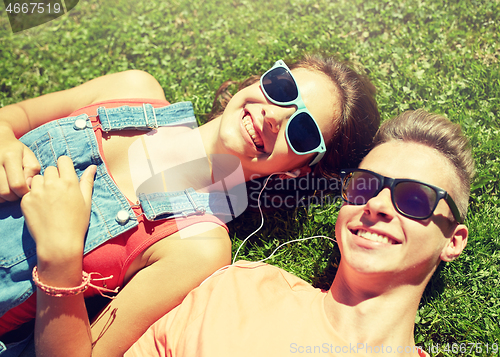 Image of happy teenage couple with earphones lying on grass