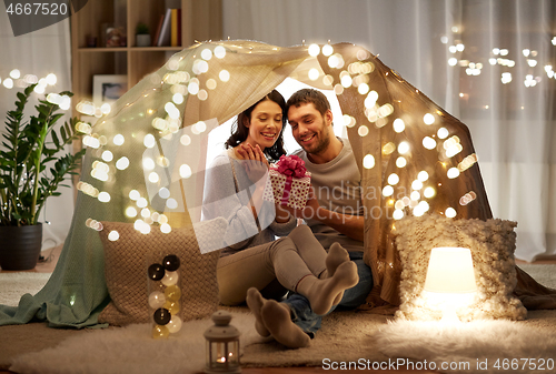 Image of happy couple with gift box in kids tent at home