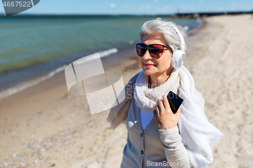 Image of old woman in headphones with smartphone on beach