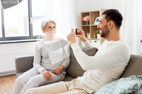 Image of adult son photographing senior mother at home