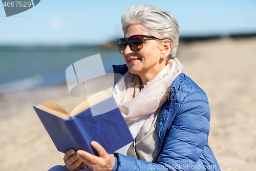 Image of happy senior woman reading book on summer beach