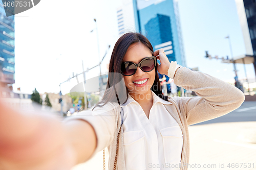 Image of smiling woman in sunglasses taking selfie in city