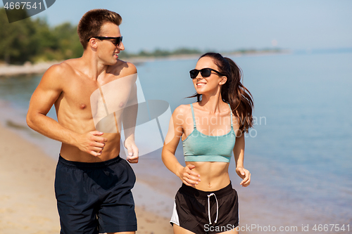 Image of couple in sports clothes running along on beach