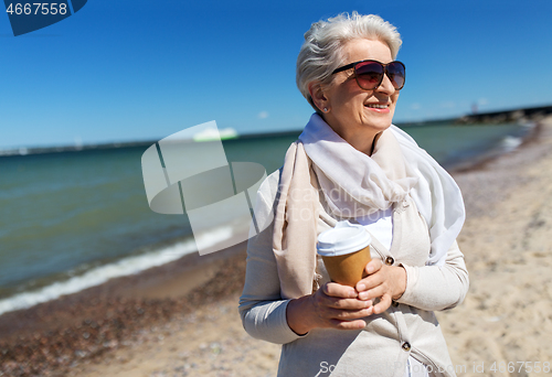 Image of senior woman drinking takeaway coffee on beach