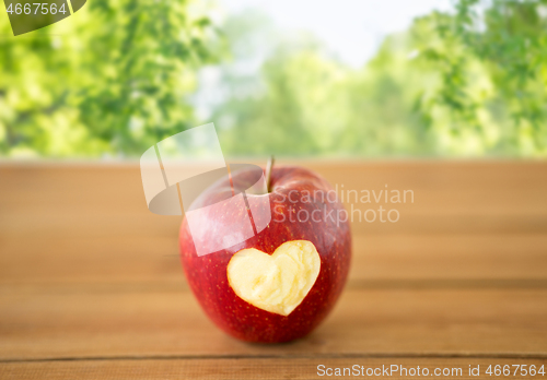 Image of red apple with carved heart shape on wooden table