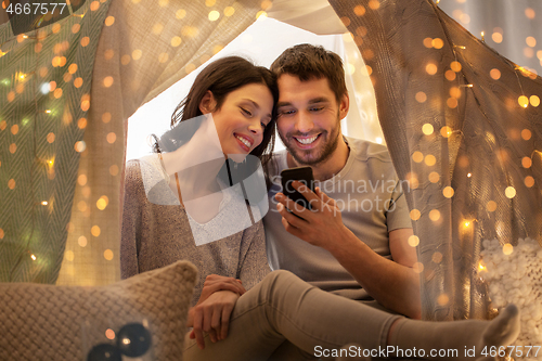 Image of happy couple with smartphone in kids tent at home