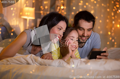 Image of happy family with smartphone in bed at night