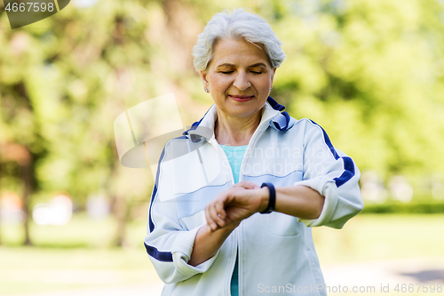 Image of sporty senior woman with fitness tracker in park