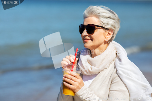 Image of senior woman drinking orange juice on beach