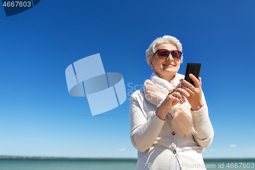 Image of senior woman using smartphone on beach