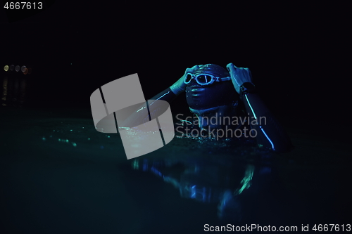 Image of authentic triathlete swimmer having a break during hard training on night neon gel light