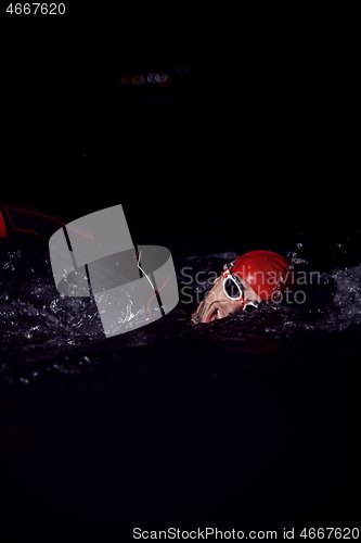 Image of triathlon athlete swimming in dark night wearing wetsuit