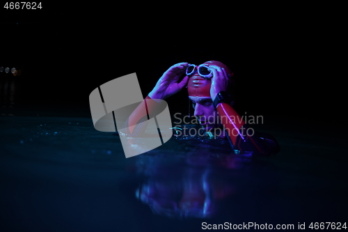 Image of authentic triathlete swimmer having a break during hard training on night neon gel light