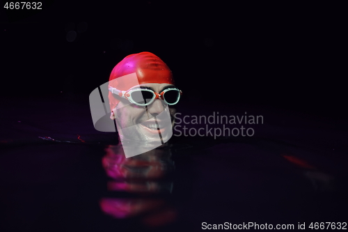 Image of authentic triathlete swimmer having a break during hard training on night neon gel light