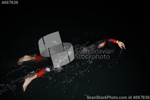 Image of triathlon athlete swimming in dark night wearing wetsuit