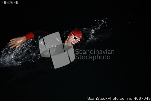 Image of triathlon athlete swimming in dark night wearing wetsuit