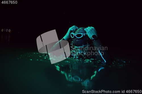 Image of authentic triathlete swimmer having a break during hard training on night neon gel light