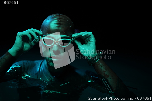 Image of authentic triathlete swimmer having a break during hard training on night neon gel light