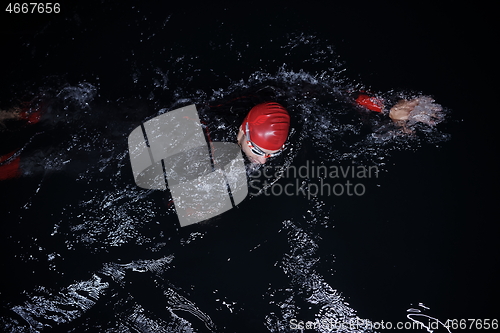 Image of triathlon athlete swimming in dark night wearing wetsuit