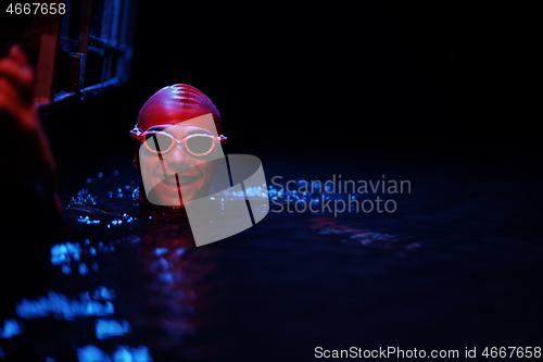 Image of authentic triathlete swimmer having a break during hard training on night neon gel light