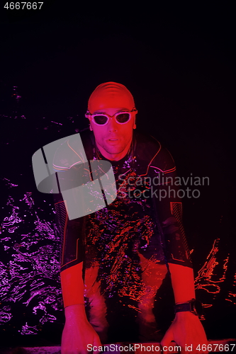 Image of authentic triathlete swimmer having a break during hard training on night neon gel light