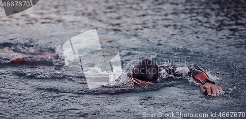 Image of triathlon athlete swimming on lake in sunrise wearing wetsuit