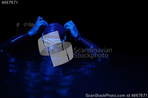 Image of authentic triathlete swimmer having a break during hard training on night neon gel light