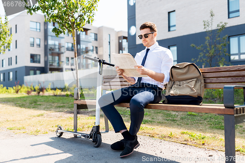 Image of businessman with scooter reading newspaper in city