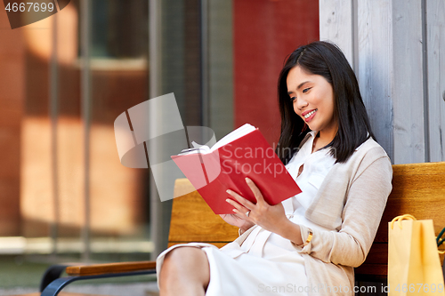 Image of smiling asian woman reading book sitting on bench