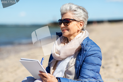 Image of senior woman writing to notebook on summer beach