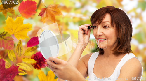 Image of smiling senior woman with mirror applying mascara