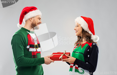 Image of happy couple in christmas sweaters with gift box