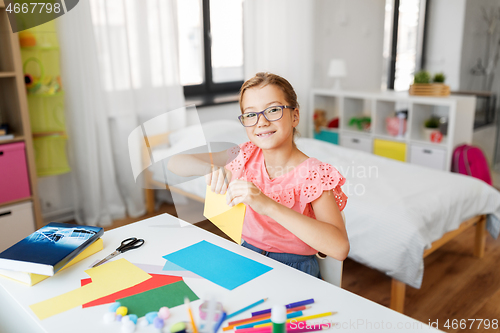 Image of girl with color paper sitting at table at home