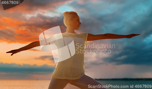 Image of woman making warrior pose over sea sunset