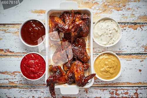 Image of Chicken wings in thick barbecue sauce with various side dips. Served on white cast iron dish