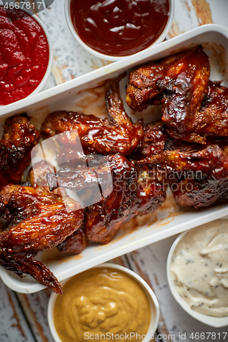 Image of Chicken wings in thick barbecue sauce with various side dips. Served on white cast iron dish