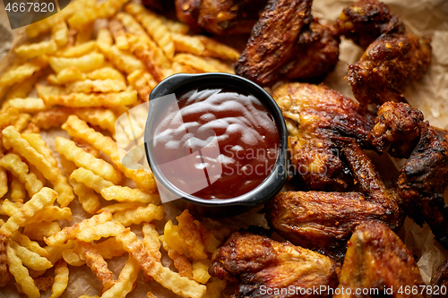 Image of Appetizing roasted chicken wings and french fries with barbecue dip, served on baking paper