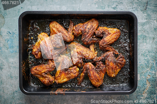 Image of Grilled chicken wings in spices in black metal baking tray on stone table. Top view