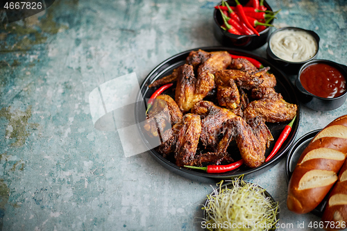 Image of Grilled chicken wings with chilli pepper on a rustic plate served with various dips and bread