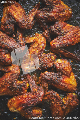 Image of Grilled chicken wings in spices in black metal baking tray on stone table. Top view