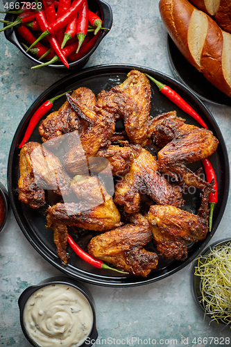 Image of Grilled chicken wings with chilli pepper on a rustic plate served with various dips and bread