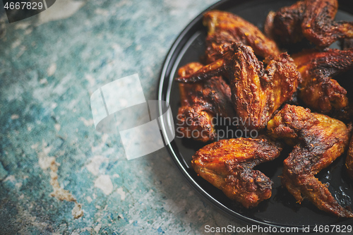 Image of Grilled chicken wings on a black ceramic plate. Placed on a stone