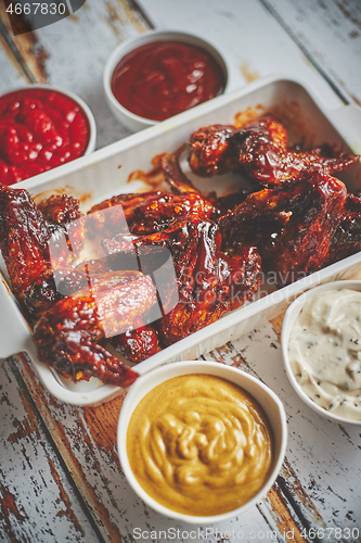 Image of Chicken wings in thick barbecue sauce with various side dips. Served on white cast iron dish