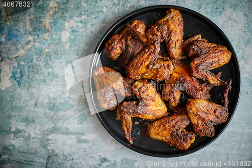 Image of Grilled chicken wings on a black ceramic plate. Placed on a stone