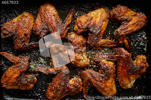 Image of Grilled chicken wings in spices in black metal baking tray on stone table. Top view